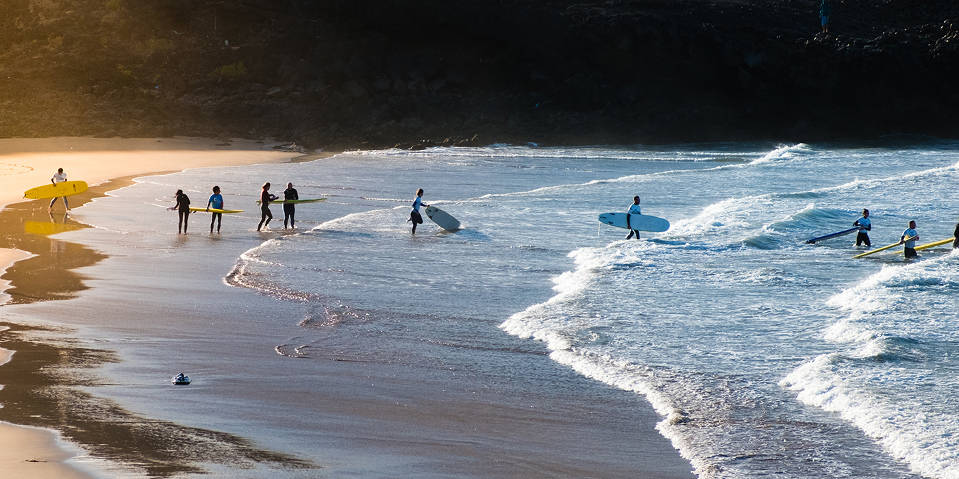 group of young people at beach going surfing